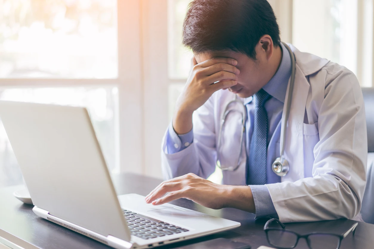 Frustrated physician dealing with a cluttered EHR interface on a laptop